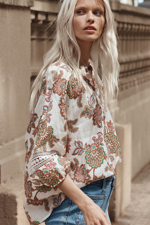 Model wears cream floral blouse and blue jeans