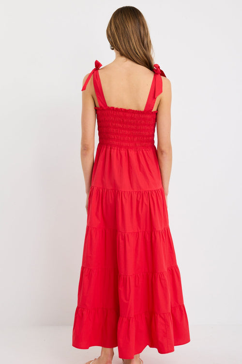 Woman wearing a cherry red tiered maxi dress with shirred bodice and strappy tie shoulders, styled with flat sandals.