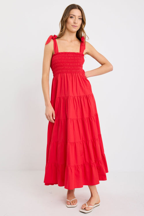 Woman wearing a cherry red tiered maxi dress with shirred bodice and strappy tie shoulders, styled with flat sandals.