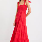 Woman wearing a cherry red tiered maxi dress with shirred bodice and strappy tie shoulders, styled with flat sandals.