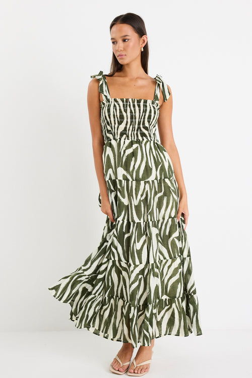 Model wearing a bold khaki zebra print dress with strappy tie details, a shirred bodice, and a tiered design. 