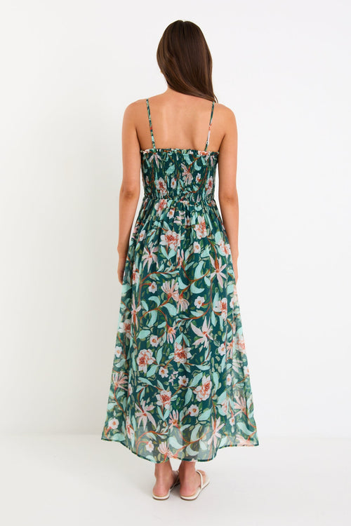 Model wearing a green forest-floral shirred midi dress with thin removable straps and a flowy skirt