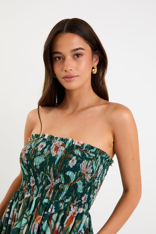 Model wearing a green forest-floral shirred midi dress with thin removable straps and a flowy skirt