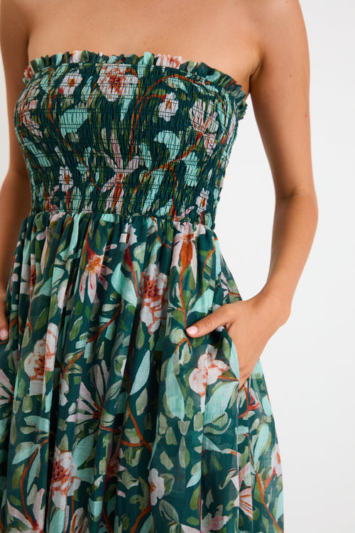 Model wearing a green forest-floral shirred midi dress with thin removable straps and a flowy skirt