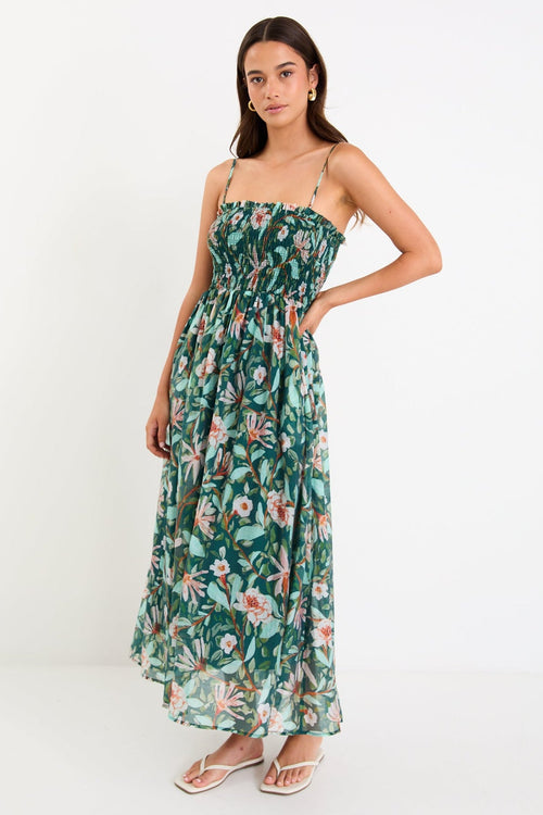 Model wearing a green forest-floral shirred midi dress with thin removable straps and a flowy skirt