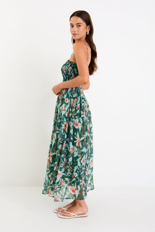 Model wearing a green forest-floral shirred midi dress with thin removable straps and a flowy skirt