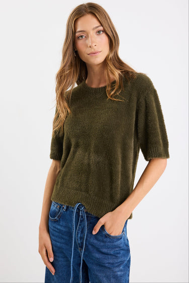 Woman wearing an olive green sweater and blue jeans on a white background