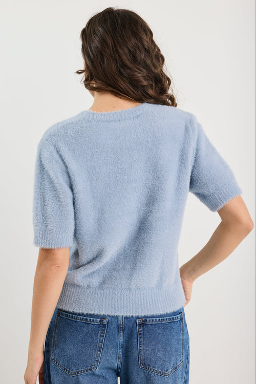 Person wearing a light blue sweater and jeans on a plain background