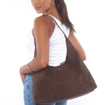 Woman wearing a white tank top and jeans, carrying a chocolate brown suede shoulder bag with a slouchy silhouette.