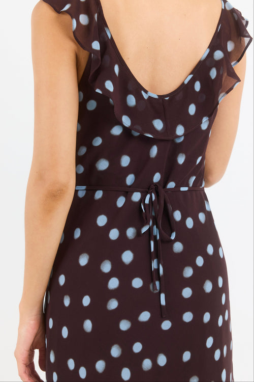 Rear view of a woman wearing a dark brown dress with a white polka dot pattern, ruffled neckline, and tie waist, against a plain white background.