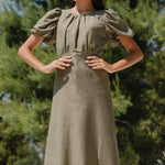 Woman wearing a green dress with puff sleeves against a natural background