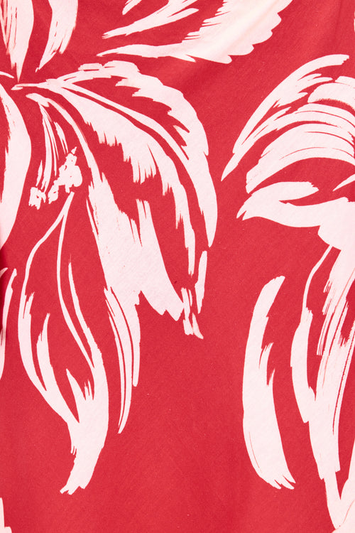 A close-up of a red fabric with a bold white tropical leaf pattern.