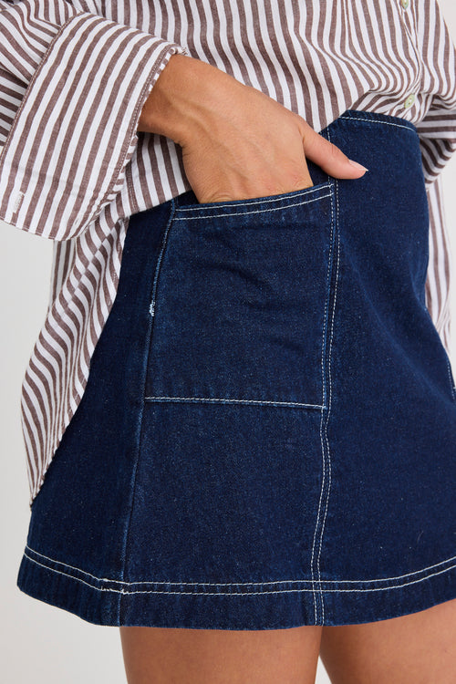 Model wears a mini denim skirt with front pockets and a shirt 