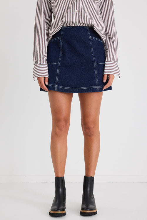 Model wears a mini denim skirt with front pockets and a shirt 