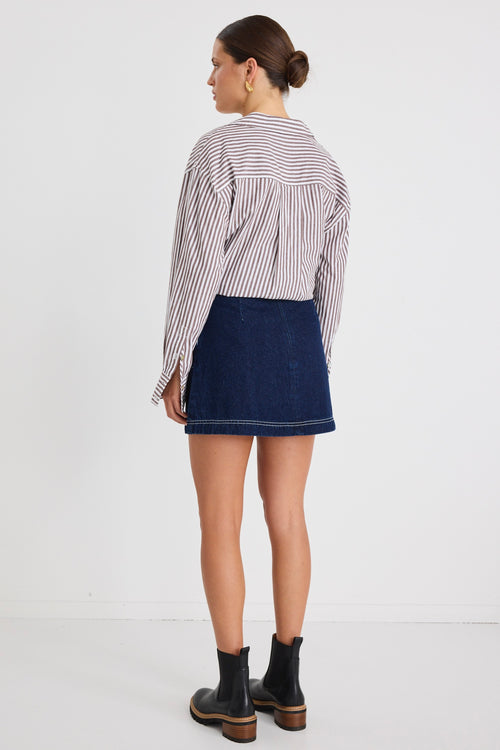 Model wears a mini denim skirt with front pockets and a shirt 