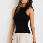 Woman wearing a sleeveless mini dress with a black shirred bodice and a natural beige flared skirt, styled simply for a casual chic look.