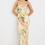 Woman wearing a cream bias-cut slip dress with peach floral print, featuring thin straps, a cowl neckline, and tie-back detail, styled with minimal accessories for a romantic look.