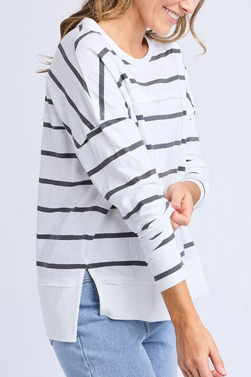 Woman wears a white long sleeve top with black horizontal stripes, crew neck, exposed stitching, and a relaxed fit. Styled with blue jeans for a casual, easy-going look.