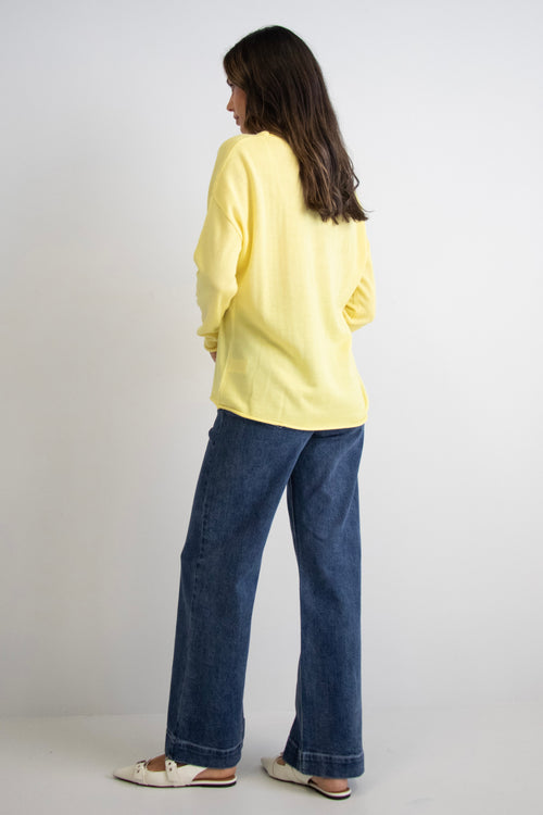 model wears a yellow knit with dark blue jeans