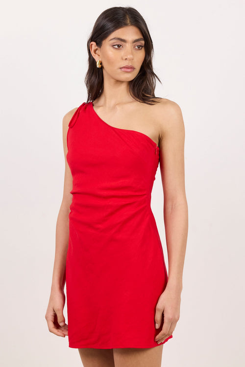 A woman modeling a bright red one-shoulder mini dress against a plain off-white studio background.