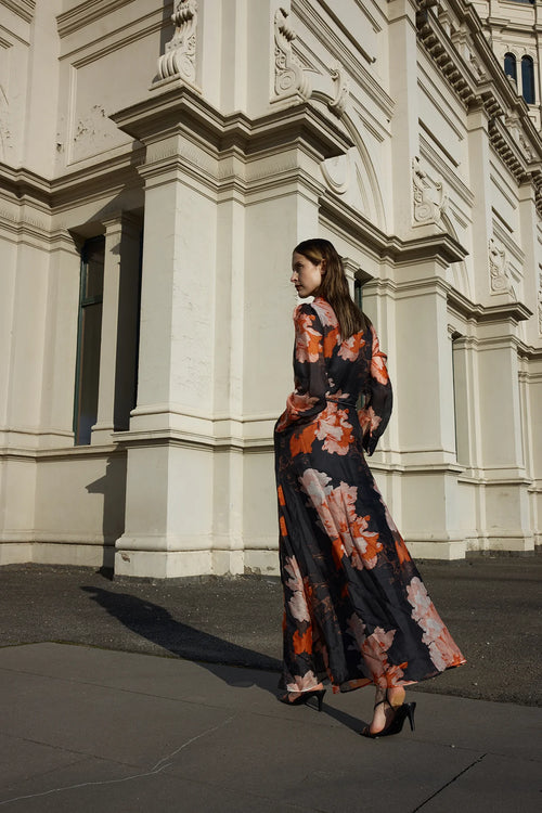 Model wears silk maxi shirt style dress with black and orange floral pattern  with tie waist 