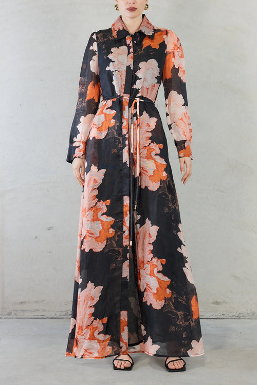 Model wears silk maxi shirt style dress with black and orange floral pattern  with tie waist 
