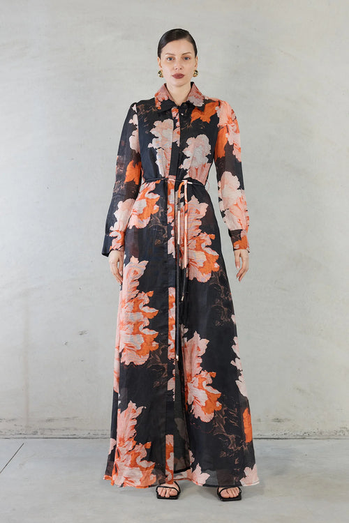 Model wears silk maxi shirt style dress with black and orange floral pattern  with tie waist 