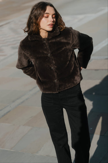 Woman wearing a brown fur coat standing on a stone pavement.