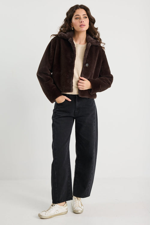Woman wearing a brown jacket and black pants on a white background