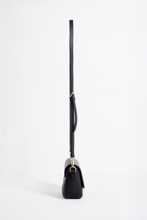 A black pebbled leather crossbody bag shown from a side profile view, featuring a long thin strap and gold-tone hardware, set against a plain white studio background.