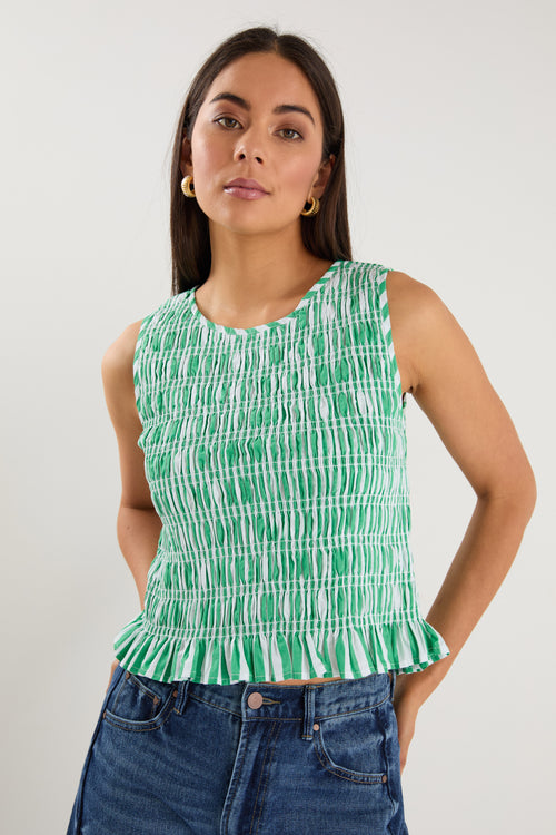 Woman wearing a sleeveless green and white striped shirred top with a peplum hem, styled with mid-blue denim jeans.