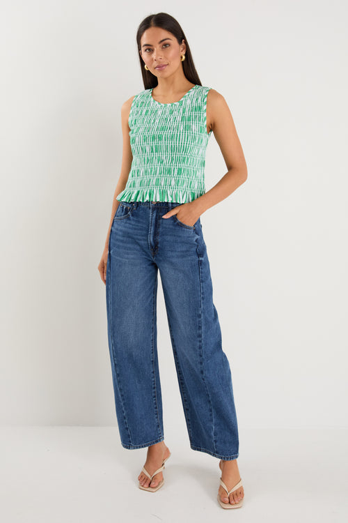 Woman wearing a sleeveless green and white striped shirred top with a peplum hem, styled with mid-blue denim jeans.