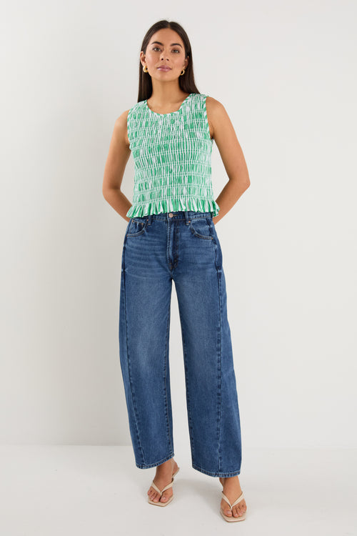 Woman wearing a sleeveless green and white striped shirred top with a peplum hem, styled with mid-blue denim jeans.