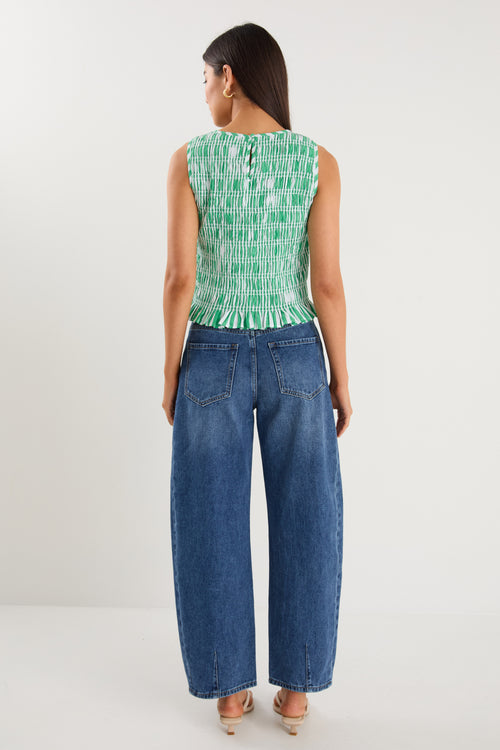 Woman wearing a sleeveless green and white striped shirred top with a peplum hem, styled with mid-blue denim jeans.