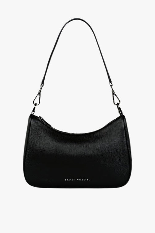 A sleek black leather crossbody bag with a soft, curved silhouette and pebble-grain texture. It features a detachable shoulder strap with silver hardware clasps and 