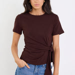Woman wearing a brown tie-front top and blue jeans against a white background