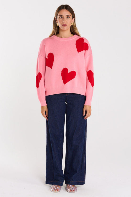Woman wearing a pink sweater with red heart patterns on a white background