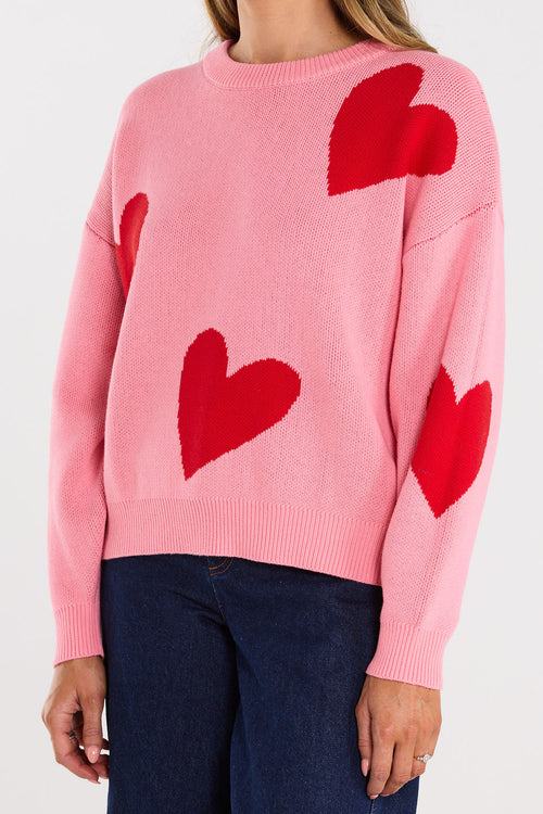 Pink sweater with red heart patterns worn by a person on a white 
background
col_pattern