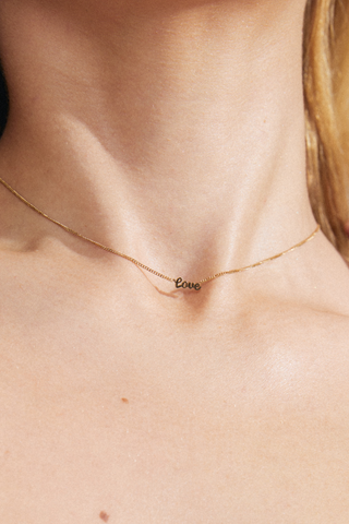 model wearing a gold chain adjustable necklace with a pendant reading "love"