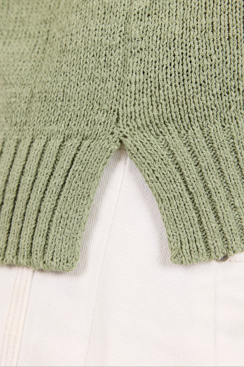 Close-up of a sage green ribbed knit garment, likely a sweater or cardigan, laid over a white fabric background.