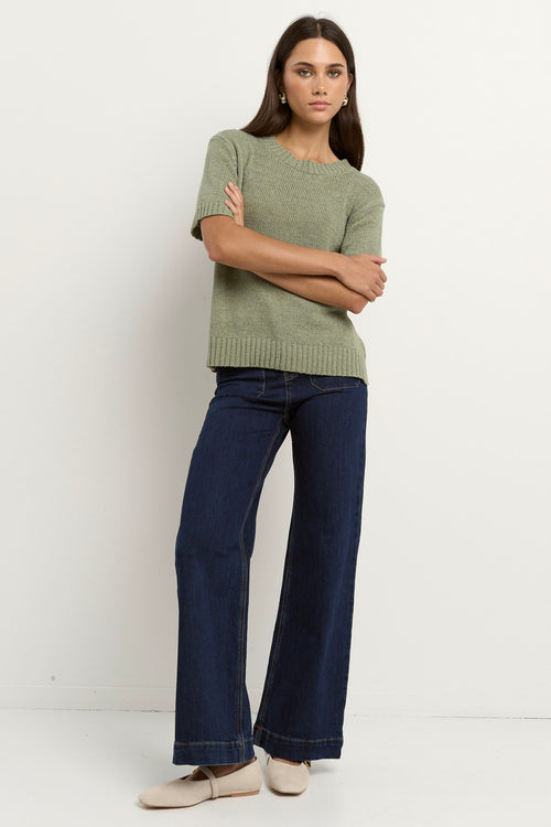Woman wearing a short sleeve sage knit top with ribbed edges and light blue jeans.