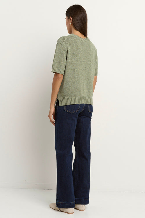 Woman wearing a short sleeve sage knit top with ribbed edges and light blue jeans.