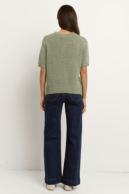 Woman wearing a short sleeve sage knit top with ribbed edges and light blue jeans.