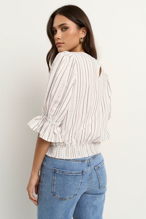 Woman wearing a puff-sleeve chocolate stripe top with shirred waist and light denim jeans.