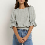 Woman wears a khaki and white striped puff sleeve top with frill detail, paired with light denim jeans.
