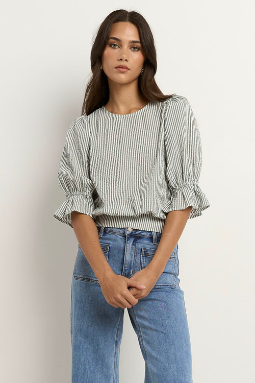 Woman wears a khaki and white striped puff sleeve top with frill detail, paired with light denim jeans.