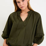 Woman wearing an olive green blouse with a plain background