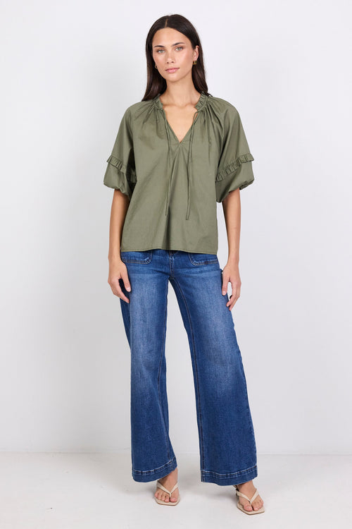Woman wearing an olive green blouse and blue jeans on a white background