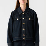 Woman wearing a dark denim jacket and pants on a white background