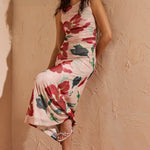Woman in a floral dress standing against a textured wall with a small table beside her.